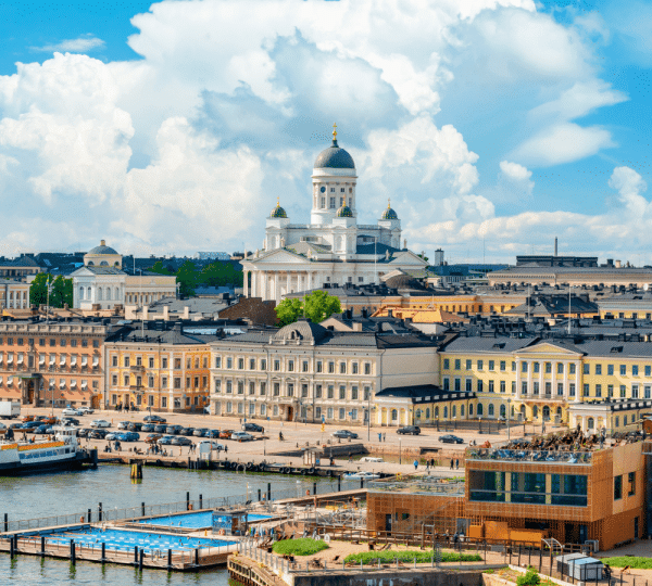 Panoramic harbor view of a European city with pastel row houses and a large domed cathedral at the center on the waterfront.